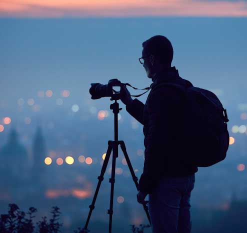 photographer with tripod and camera standing with lights in background